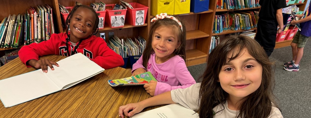 three students smiling and reading books in the library