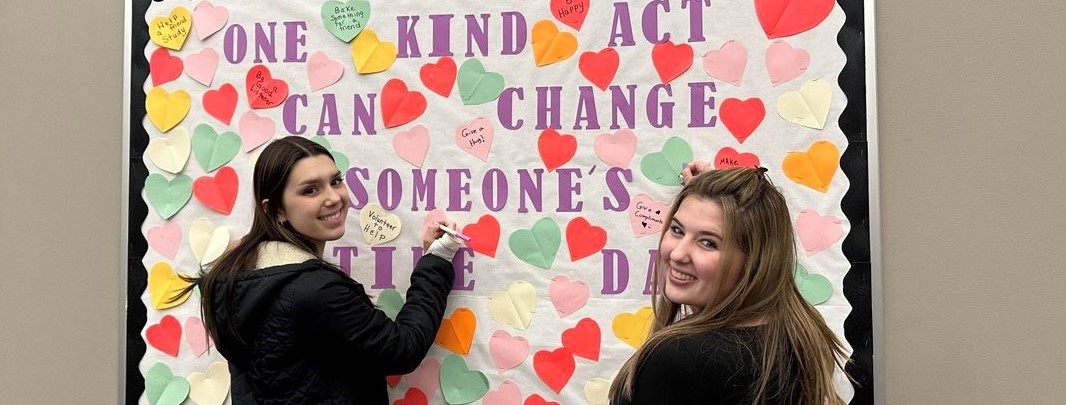 2 Girls working on bulletin board says: One kind act xan change someone&#39;s entire day