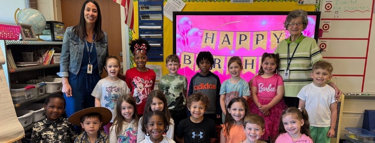 First grade students in a group photo with a volunteer who celebrated her 90th birthday with them